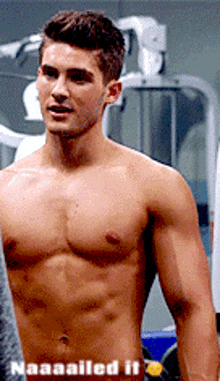 a shirtless man is standing in a gym next to a machine with the words naaaailled it written below him