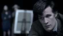 a man in a suit and bow tie is sitting in a dark room looking at something .