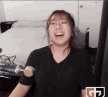 a woman is laughing in front of a microphone with the letter g on the bottom