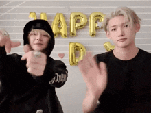 two young men are clapping in front of balloons that spell out happy day