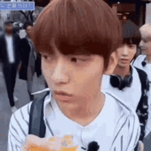 a young man wearing headphones and a striped shirt is holding a bottle of orange juice .