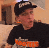 a man wearing a hooters t-shirt and a hat is making a funny face