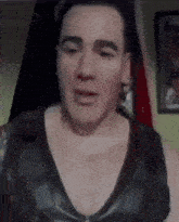 a man with a tattoo on his chest is wearing a black tank top and making a face .