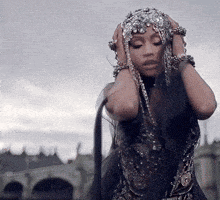 a woman wearing a headdress with rhinestones on it holds her hands to her head