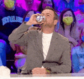 a man drinking from a can in front of a crowd wearing face masks