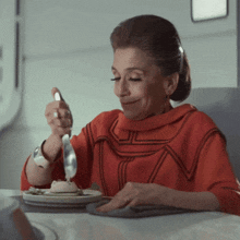 a woman in a red sweater is sitting at a table with a plate of food and a fork