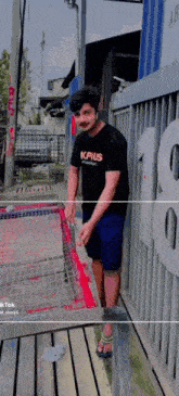 a man wearing a t-shirt that says kapus is standing in front of a fence