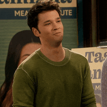 a man in a green sweater is standing in front of a sign that says meacute