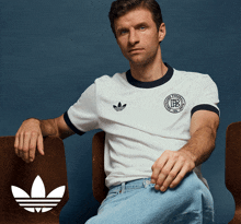 a man wearing a white adidas shirt is sitting on a chair