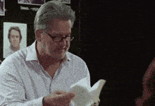 a man wearing glasses is holding a piece of paper in his hand .