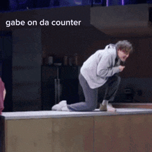 a man is kneeling on a counter with the words gabe on da counter above him .