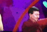a man in a red shirt is covering his mouth with his hand in front of a purple background
