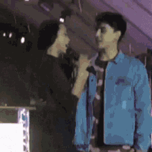 a man in a blue jacket is talking into a microphone while a woman stands next to him .