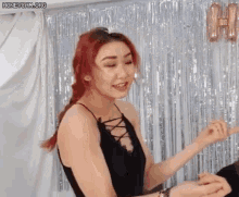 a woman with red hair is standing in front of a tinsel curtain and smiling .