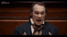 a man in a suit and bow tie is giving a speech in a parliament .