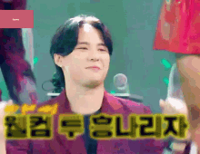 a man in a purple suit is smiling in front of a microphone with korean writing on it .
