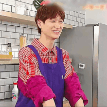 a man wearing a purple apron and a plaid shirt smiles in a kitchen