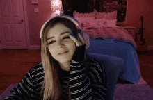 a woman wearing headphones looks at the camera in a bedroom
