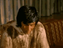 a man is sitting on a couch wearing a dirty sweater .