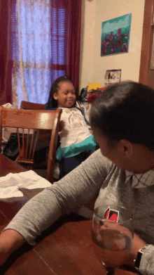 a woman sits at a table with a glass of water and a little girl sitting on her lap