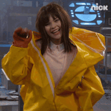 a woman wearing a yellow jacket and orange gloves is smiling for the camera with the nick logo in the background