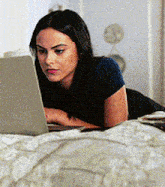 a woman is laying on a bed looking at a laptop