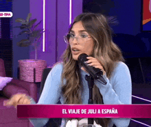 a woman wearing glasses is talking into a microphone with the words el viaje de juli a espana on the bottom