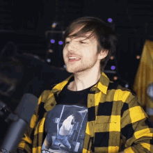 a man wearing a yellow and black plaid shirt and a black t-shirt with a picture of a person on it