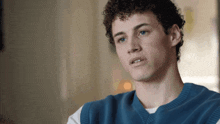 a man with curly hair wearing a blue vest