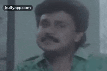 a man with a mustache is looking at the camera with a blurred background and the words kulfyapp.com in the corner