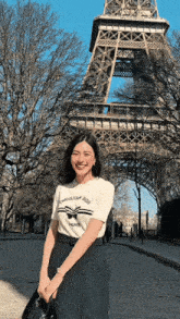 a woman standing in front of the eiffel tower wearing a christian dior t-shirt