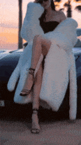 a woman wearing a white fur coat is sitting on the side of a car