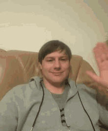 a man in a gray hoodie is sitting on a brown leather couch .