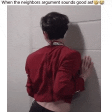 a man in a red shirt is leaning against a wall with his back to the camera .