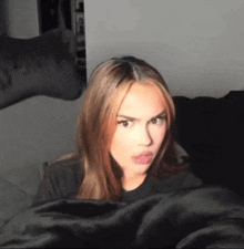 a young woman with long brown hair is making a funny face while laying on a bed .