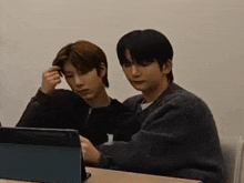 two young men are sitting at a table looking at a laptop .