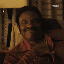 a man in a red shirt sits in a chair with a max logo in the background