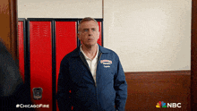 a man in a blue jacket with the word chicago on it stands in front of red lockers
