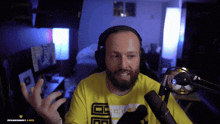 a man with a beard wearing headphones and a yellow shirt with the letter e on it talks into a microphone