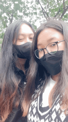 two girls wearing black face masks and glasses pose for a picture