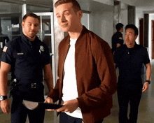 a man in a brown jacket is standing in front of two police officers .