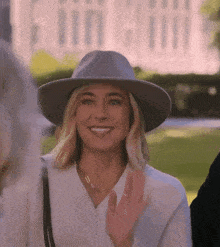 a woman wearing a hat and a necklace is smiling and waving