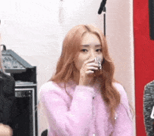a woman in a pink sweater is drinking from a glass while sitting in front of a microphone .