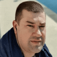 a man wearing a blue shirt and ear buds looks at the camera