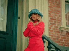 a woman wearing a blue hat and a red jacket stands on a set of stairs