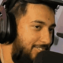a man with a beard wearing headphones and a hat is smiling into a microphone .