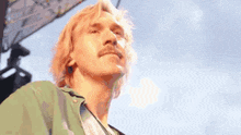a man with blonde hair and a mustache is looking up at the sky .