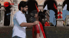 a man and woman are kissing in front of a building with a red circle that says zee
