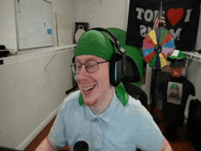 a man wearing headphones and a green headband smiles in front of a sign that says " i love tom "