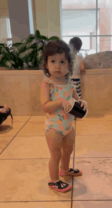 a little girl in a bathing suit holds a black cup
